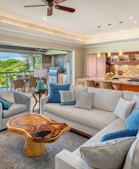 A modern living room with a white sofa, wooden coffee table, open kitchen, and outdoor patio with seating and a barbecue grill.