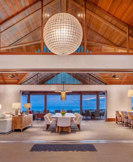 A luxurious open-concept living and dining area features wooden ceilings, modern furniture, a large chandelier, and a sea view through large windows.