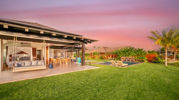 A luxurious outdoor setting with a spacious patio, swing, dining area, lush lawn, palm trees, and a pool, all under a beautiful pink sky.