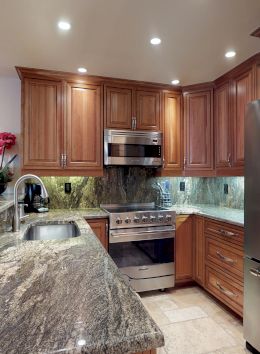 A modern kitchen with wooden cabinets, granite countertops, stainless steel appliances, decorative items, and recessed lighting.