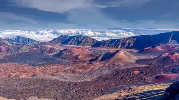 The image shows a stunning volcanic landscape with mountains, colorful volcanic cinder cones, and a sky with clouds in the background.