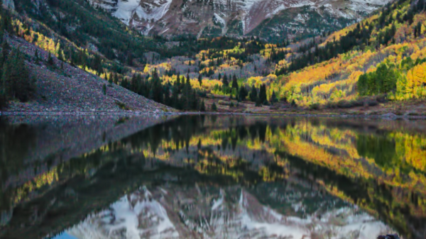 A serene mountain landscape with snow-capped peaks reflected in a calm lake, surrounded by autumn-colored trees under a clear, starry sky.