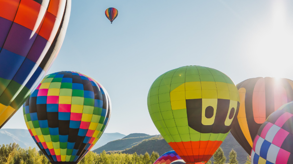 A vibrant scene featuring multiple colorful hot air balloons at a festival on a sunny day, with people gathered around and mountains in the background.