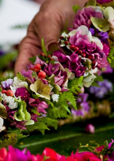 A hand is holding a colorful garland made of various flowers and green leaves, showcasing intricate floral arrangements.