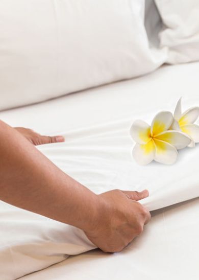 A person making a bed with white sheets, adorned with two white and yellow frangipani flowers on top.