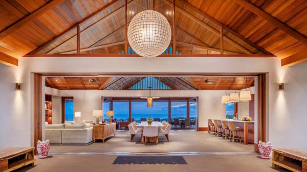 Spacious open-concept living and dining area with wooden ceilings, a large globe chandelier, and a view of the ocean through wide glass doors.