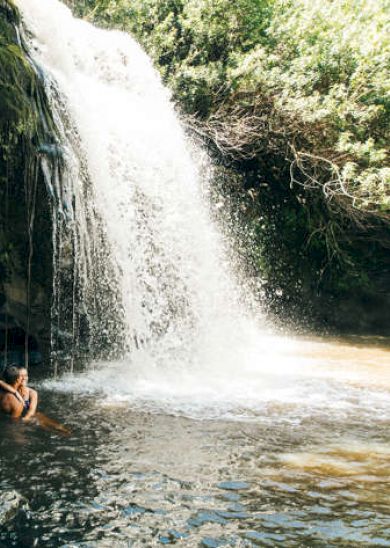 A person swings on a rope by a waterfall, surrounded by lush greenery and a pool of water below.