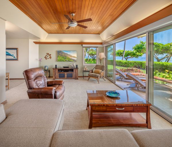 A cozy living room with a mix of modern and rustic decor, featuring large windows overlooking a lush garden and ocean views, plus outdoor seating.