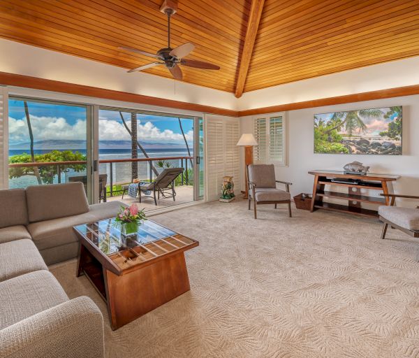 A cozy living room with a beige sectional, glass coffee table, armchairs, and a scenic ocean view through sliding glass doors leading to a balcony.