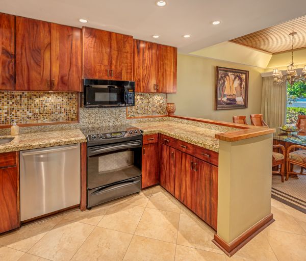 An elegant kitchen with wood cabinets, granite countertops, a black stove, a dishwasher, and a mosaic backsplash near a dining area with a chandelier.