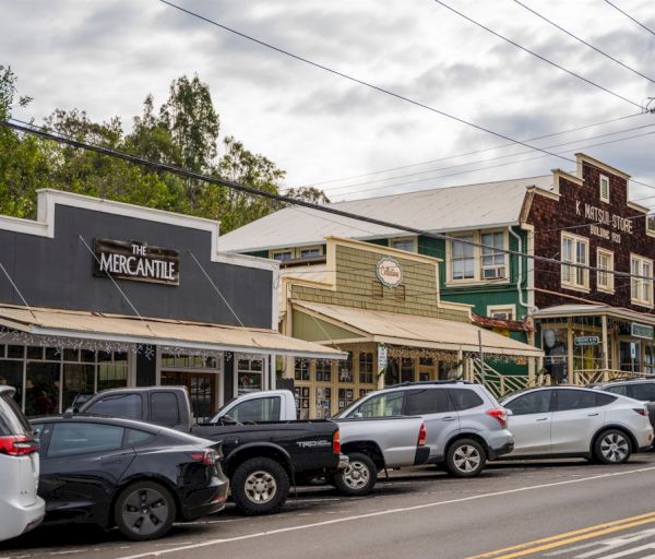 The image shows a row of buildings with storefronts including "The Mercantile," and several parked cars along the street.