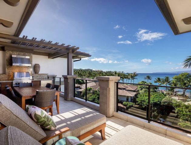 A luxurious terrace overlooking the ocean, featuring lounge chairs, a dining table, and an outdoor kitchen area under a pergola.