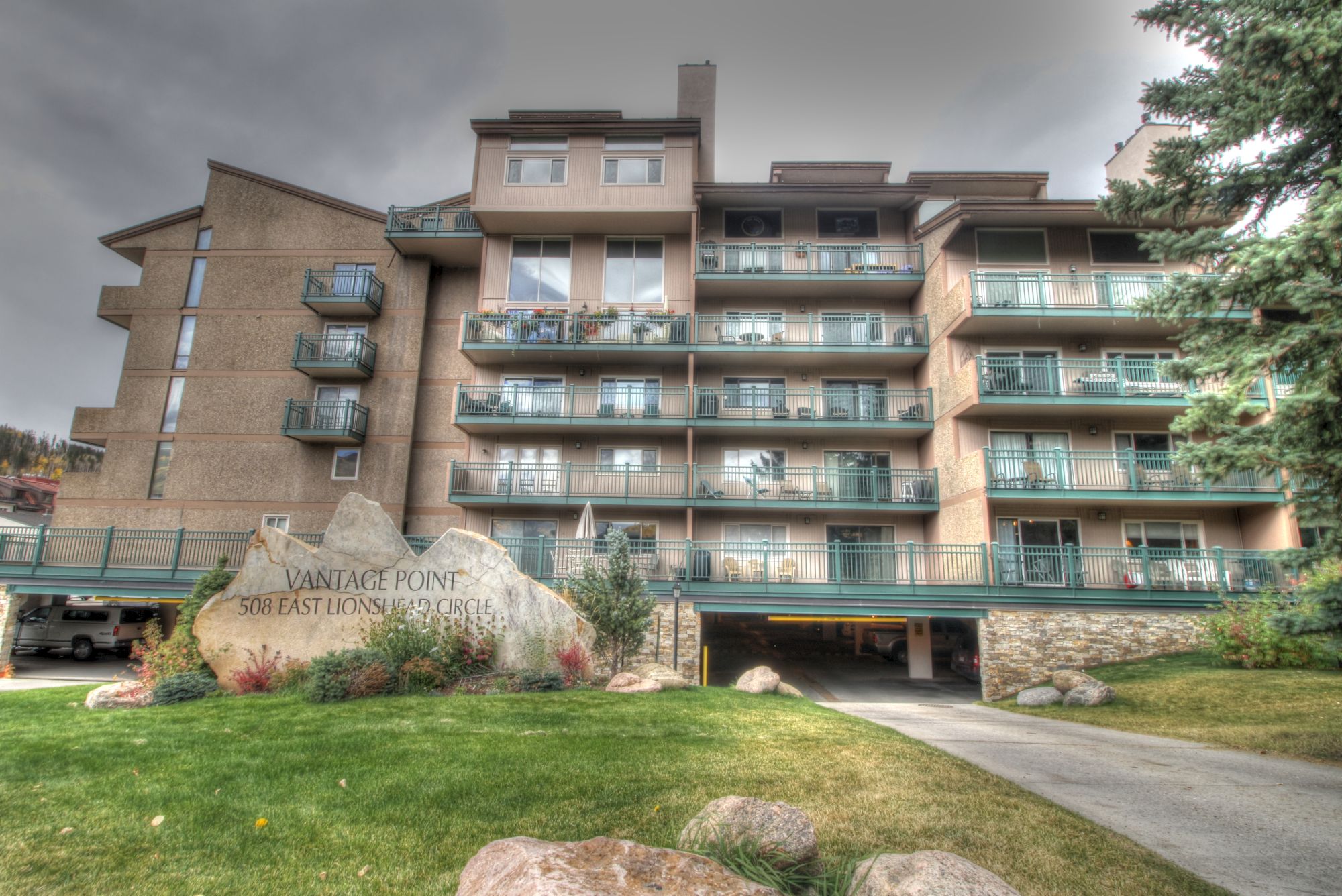 The image shows a multi-story building with balconies, a grassy lawn with rocks, and a sign that reads "Vantage Point" in front of the building.